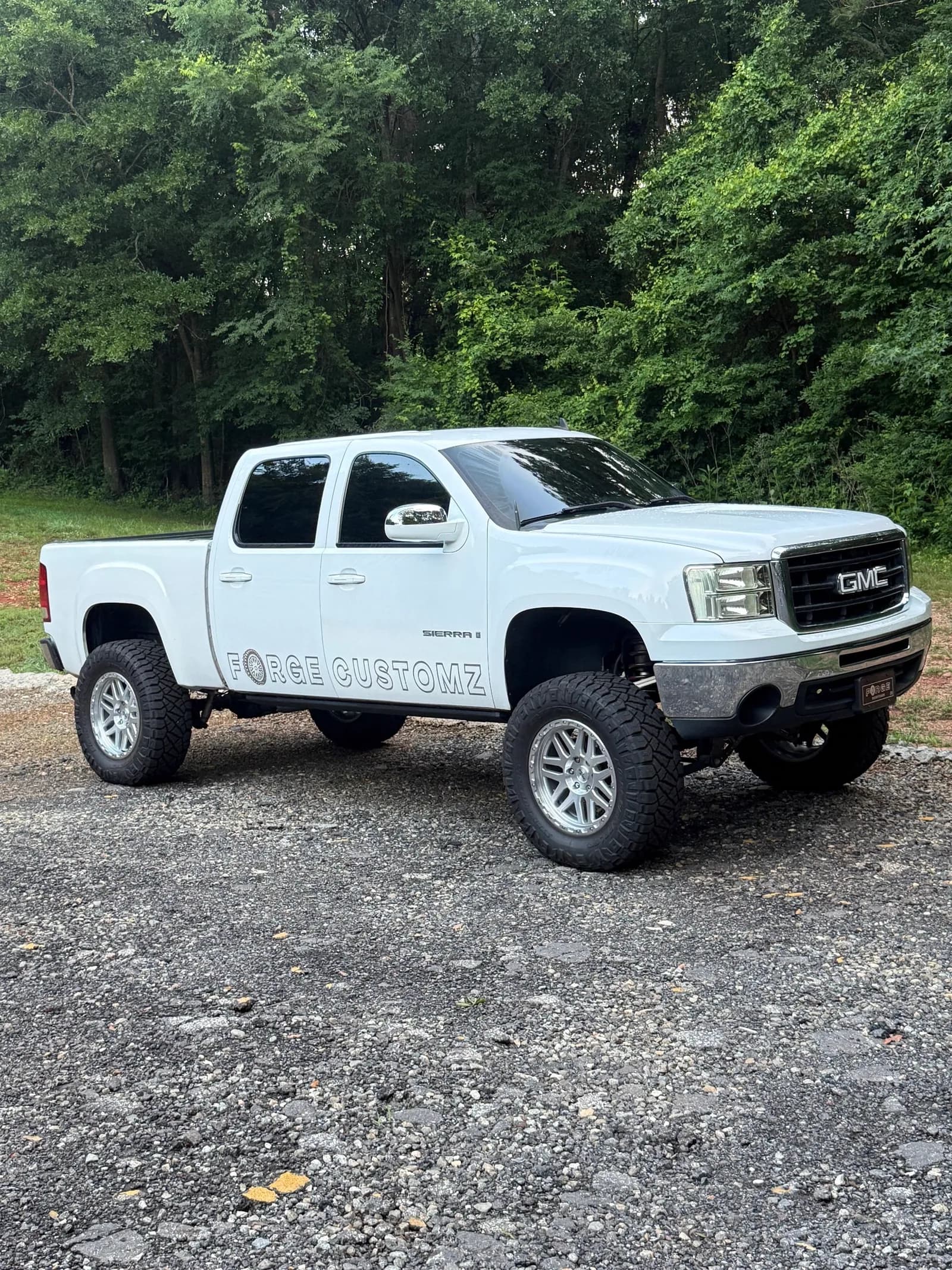 White GMC Sierra on a lift kit with Forge Customz lettering down the side